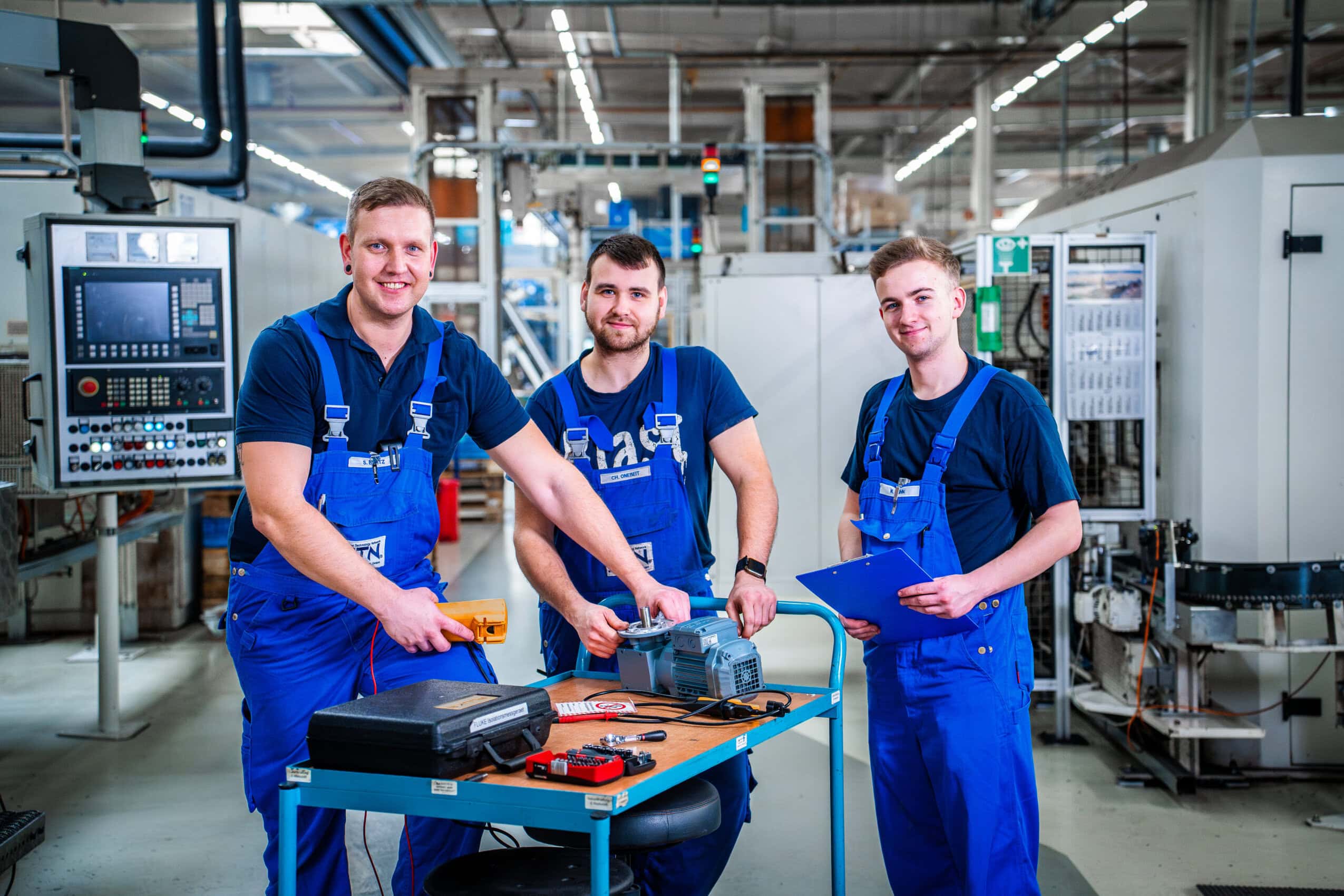 3 Kollegen am Werkzeugwagen Technikerteam der NTN Antriebstechnik GmbH in Gardelegen bei elektrischer Prüfung an mobiler Werkstation in moderner Fertigungsumgebung.
